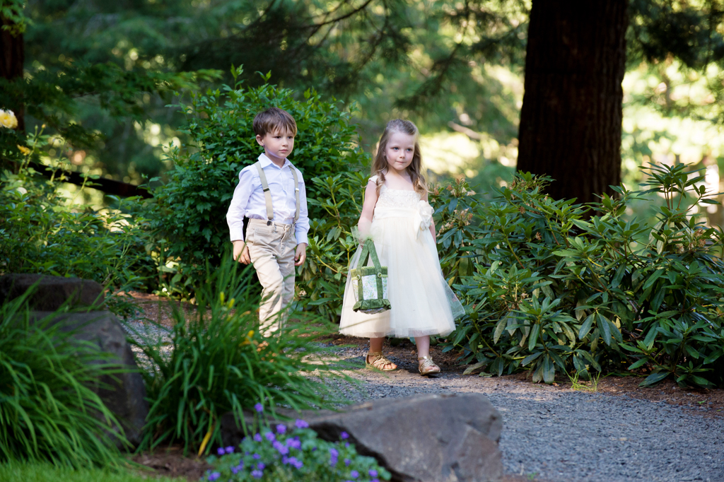 a flower girl and ring bearer walk down the trail toward the wedding ceremony