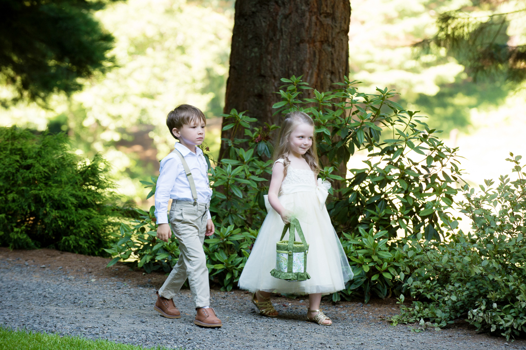 a flower girl and ring bearer walk down the trail toward the wedding ceremony