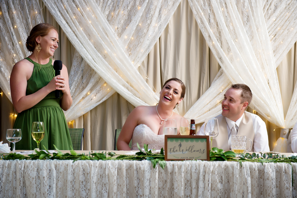 bride and groom laugh as maid of honor gives wedding reception toast
