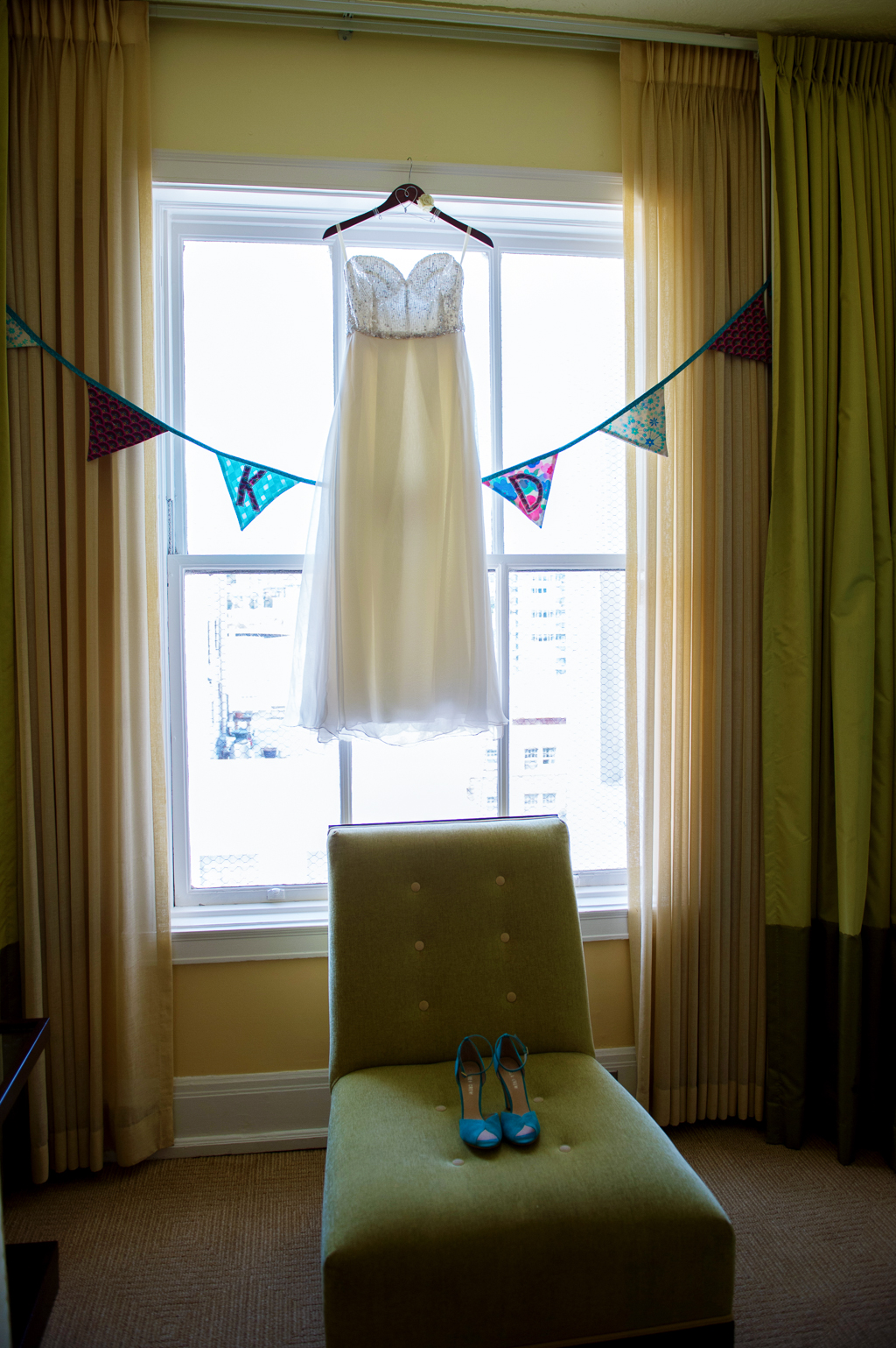 wedding dress hangs from window in hotel deluxe with colorful bunting around it