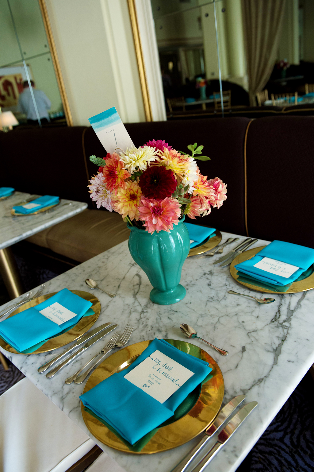 teal vintage vases hold orange yellow salmon and dark red colored flowers on a table with gold plates and turquoise napkins