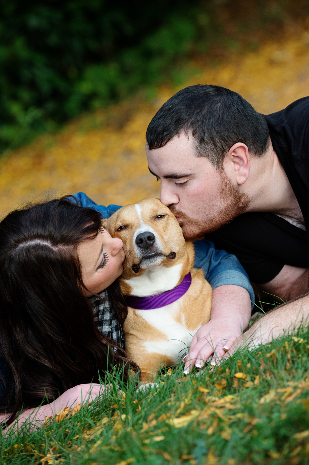 a man and woman lay on either side and kiss their dog