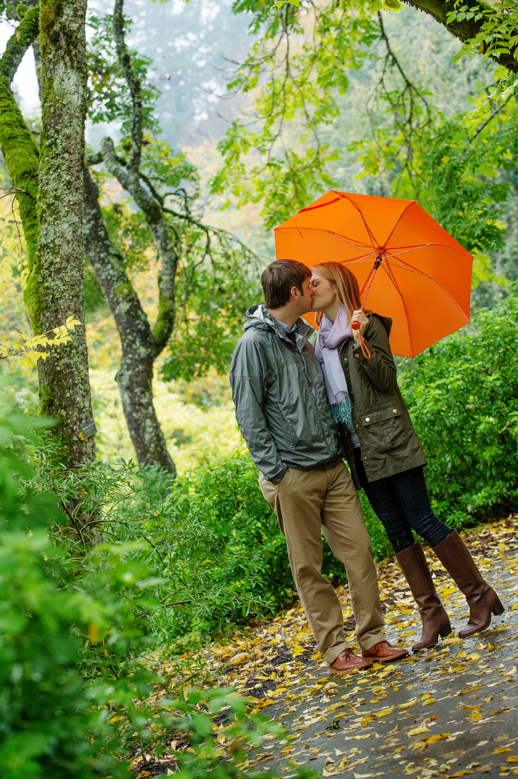 a couple kiss under an orange umbrella on a rainy day