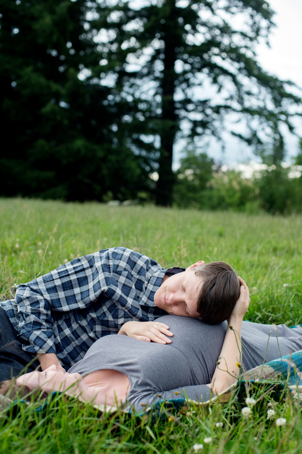 a man lays his head on a pregnant woman's belly as they lay in the grass at hoyt arboretum