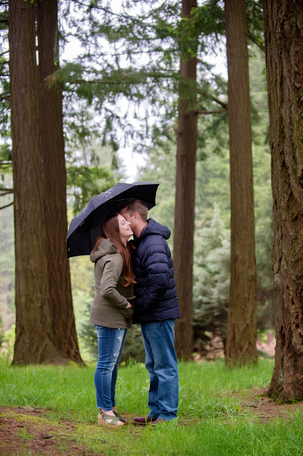 a couple hug under an umbrella surrounded by tall trees