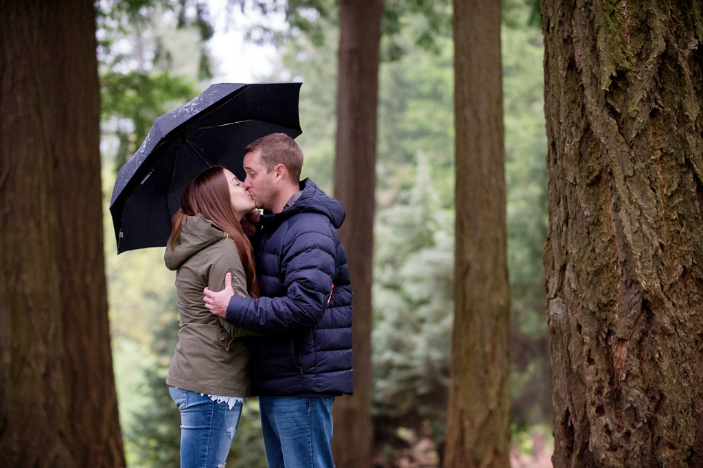 a couple hug under an umbrella surrounded by tall trees