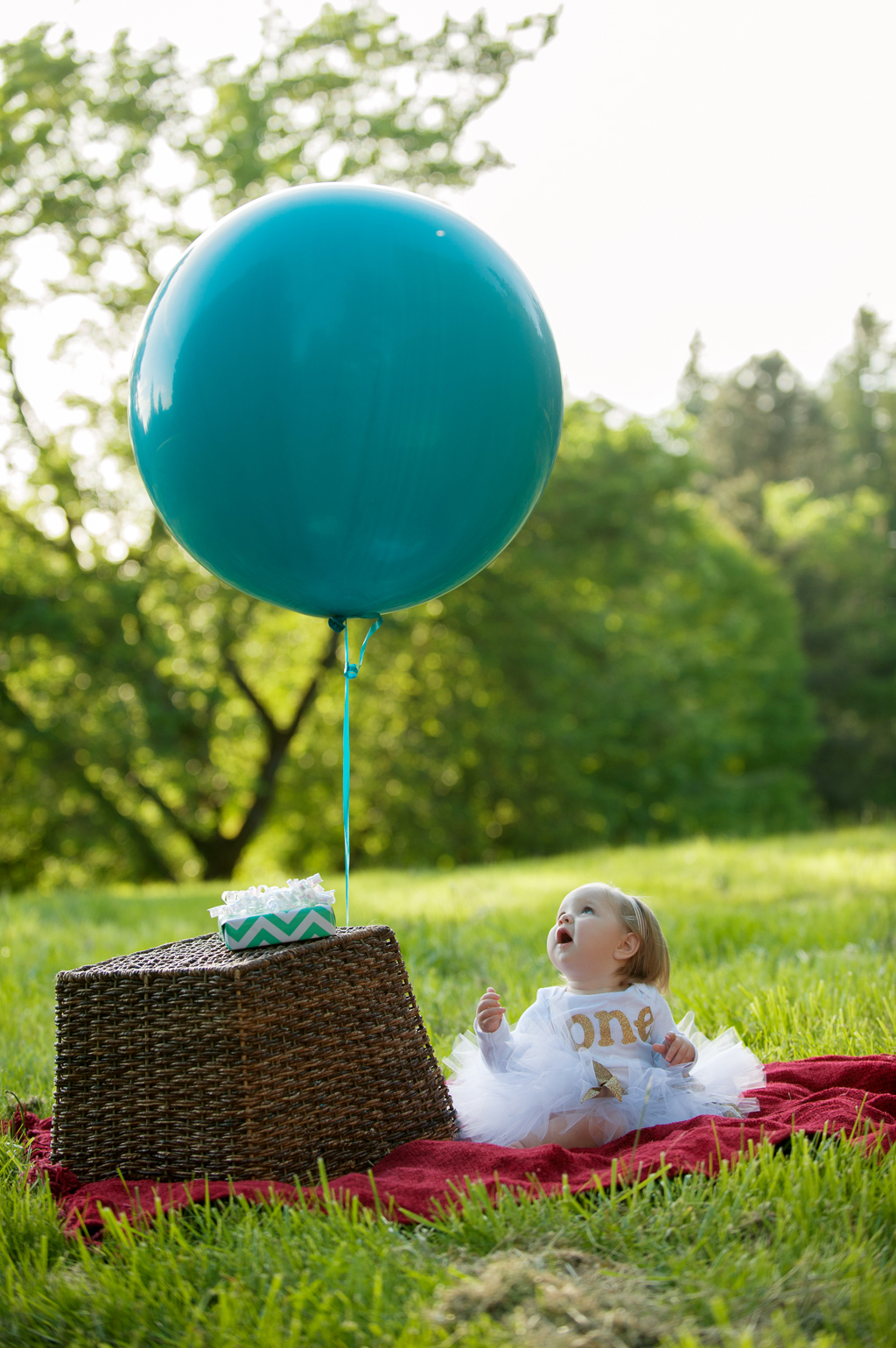 a baby girl wearing a white tutu looks up at a giant blue balloon