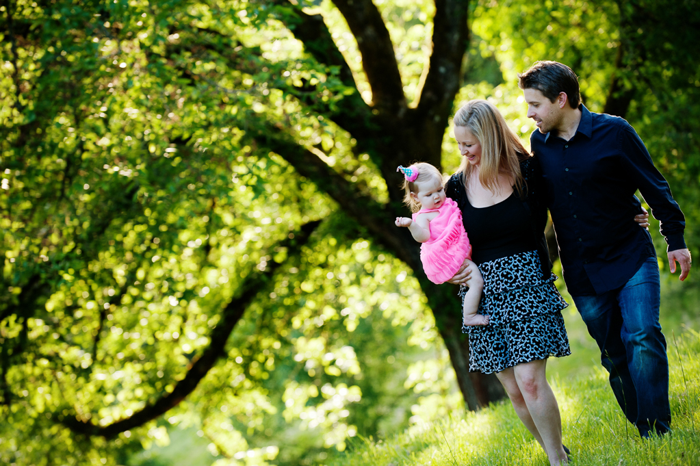 a mom and dad walk through hoyt arboretum carrying their baby girl wearing a hot pink dress