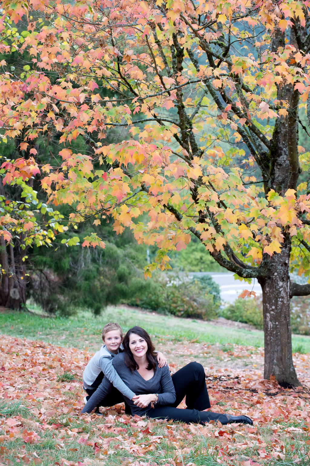 a mother and her son embrace while sitting in a pile of leaves