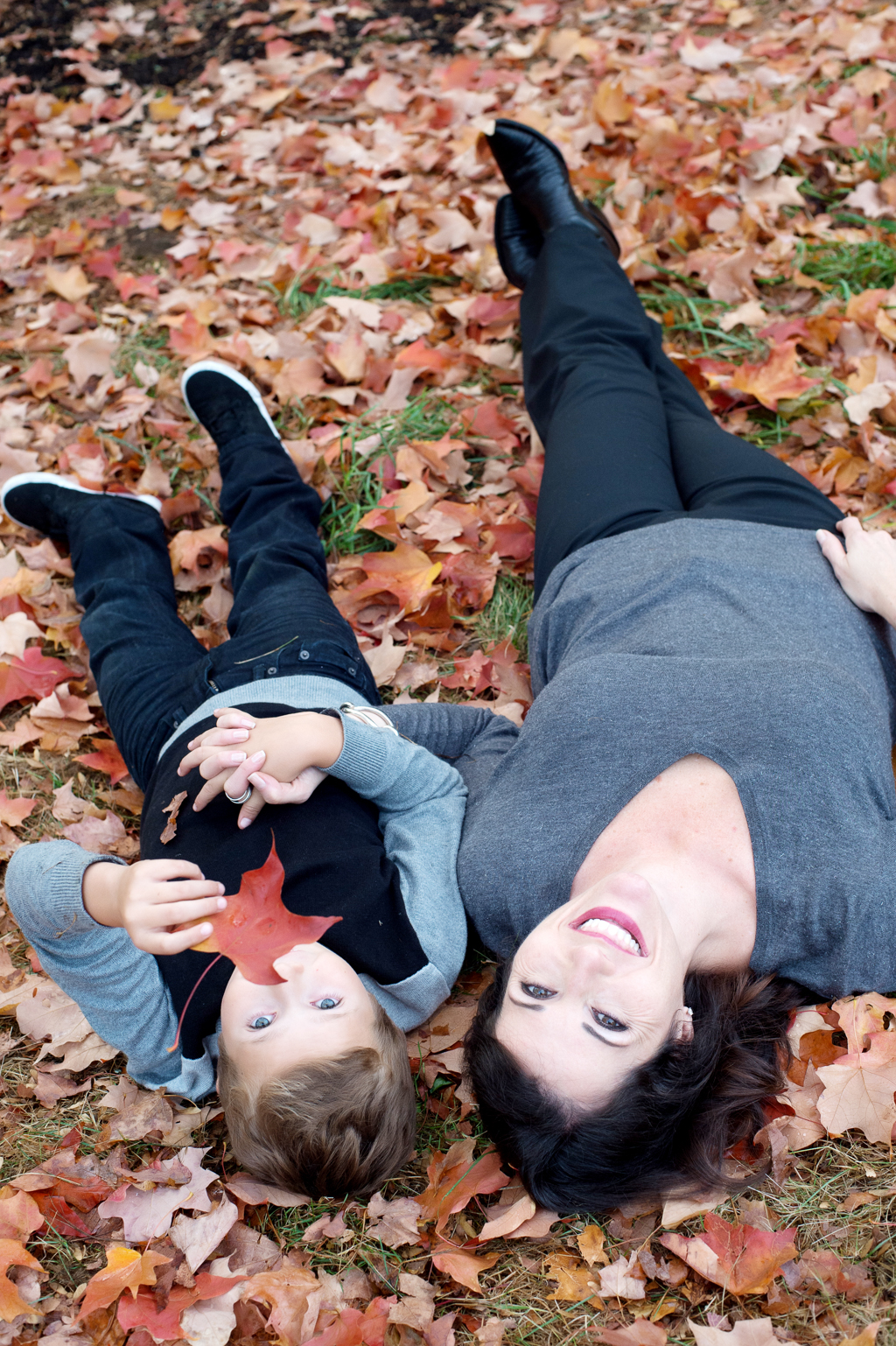a mother and son lay in colorful red autumn leaves