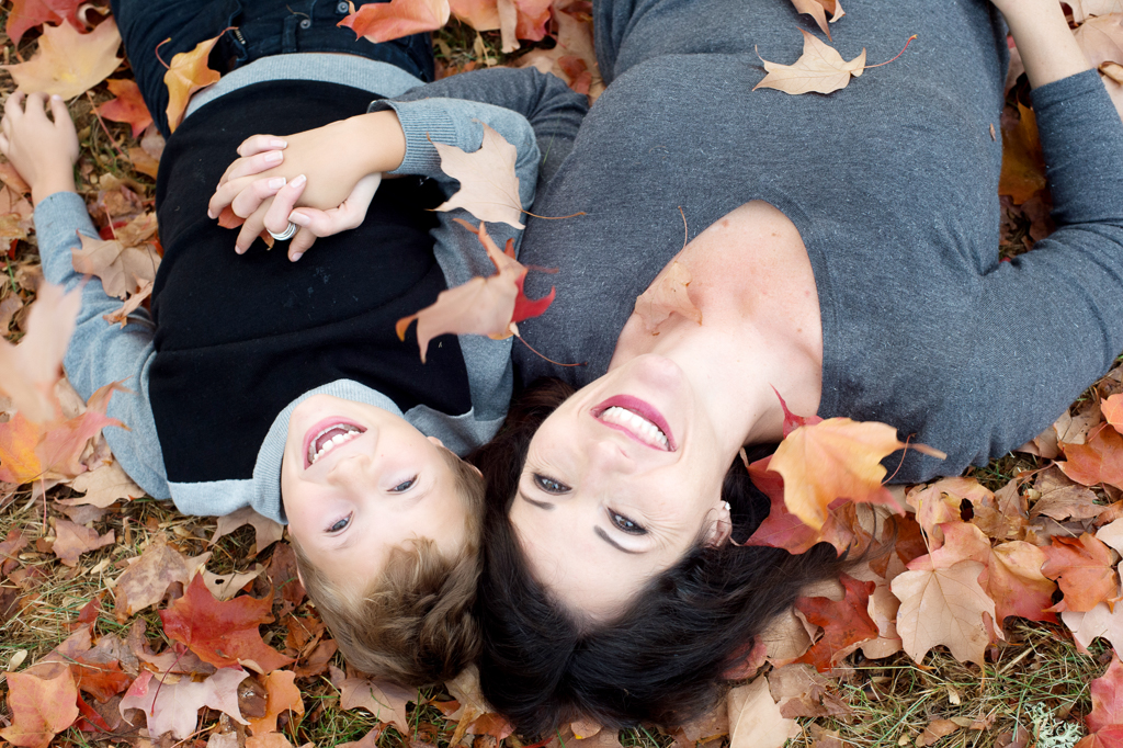 a mom and son lay in colorful autumn leaves