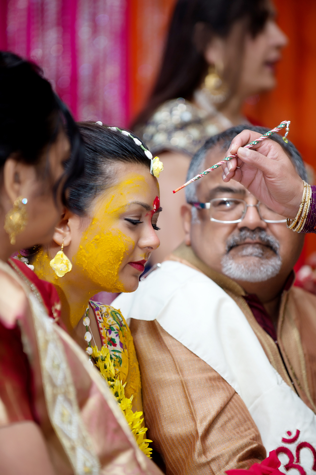 a red paste is applied to bride's forehead during the turmeric ceremony at her indian wedding