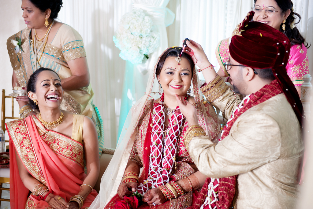 an indian groom applies powdered red lead to bride's head during the sindhoor ceremony