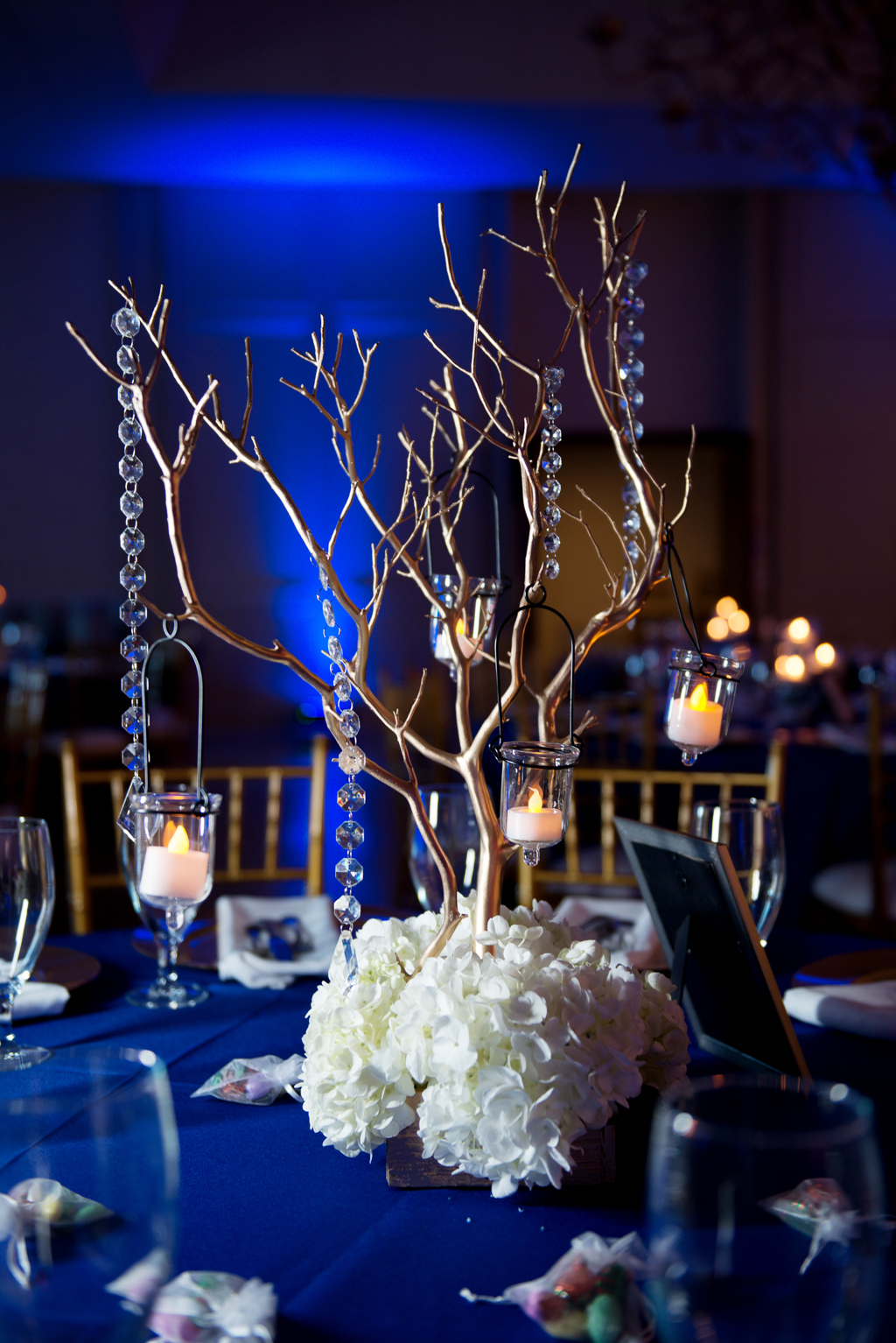 dark blue and white hydrangeas decorate wedding reception with dark blue uplighting in background