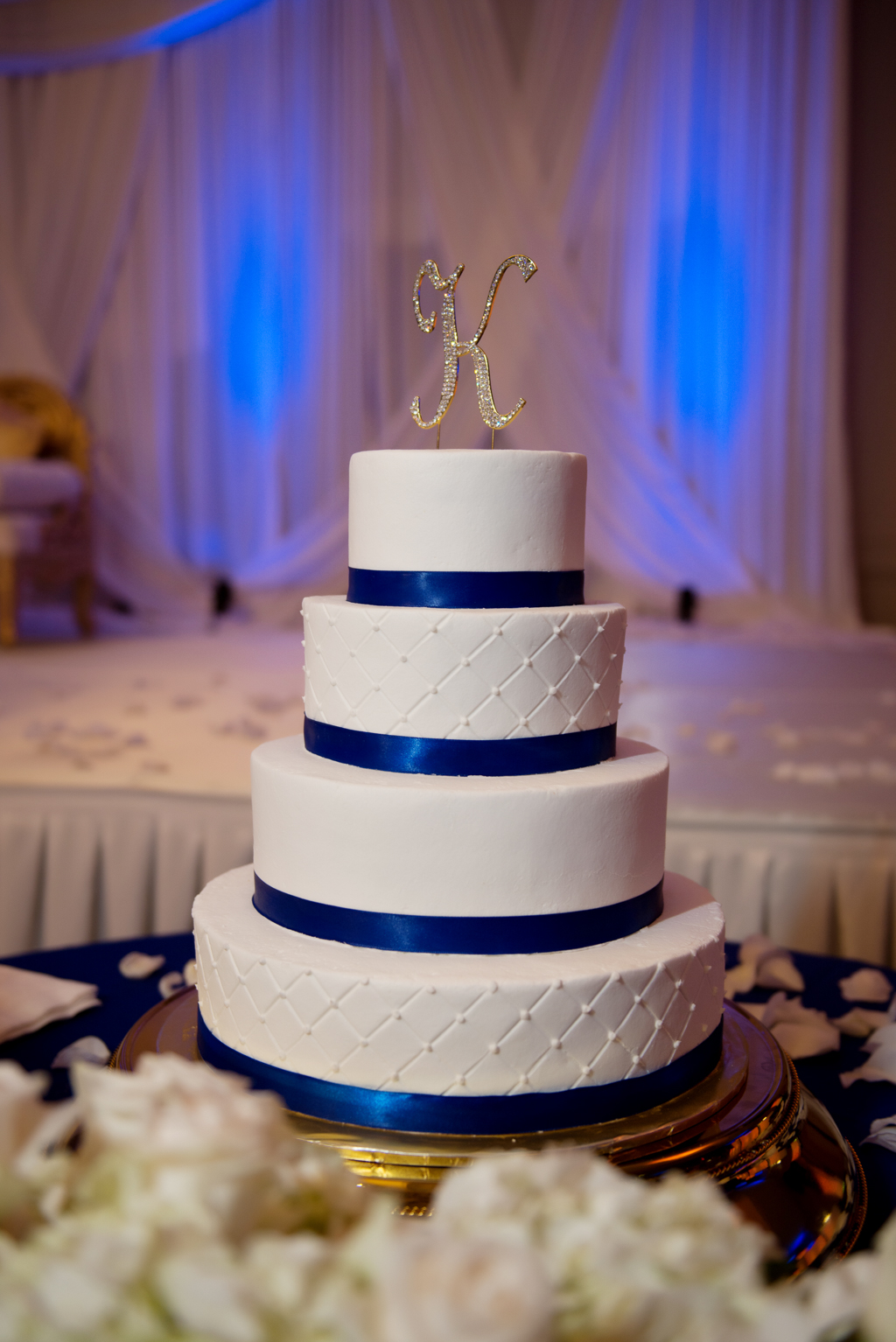 a navy and white wedding cake with royal blue uplighting in background