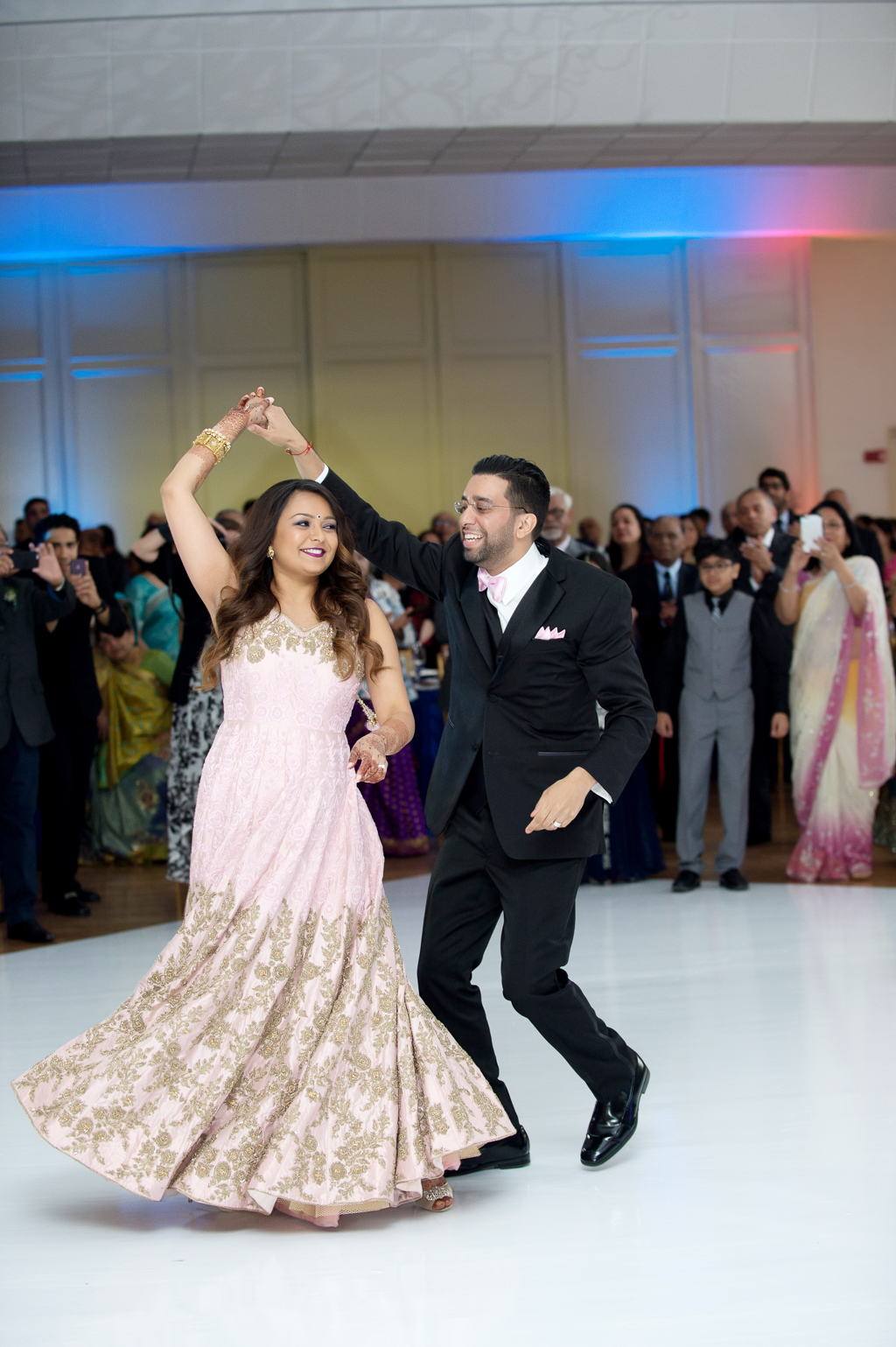 an indian bride wears a pink and gold dress during the couple's first dance