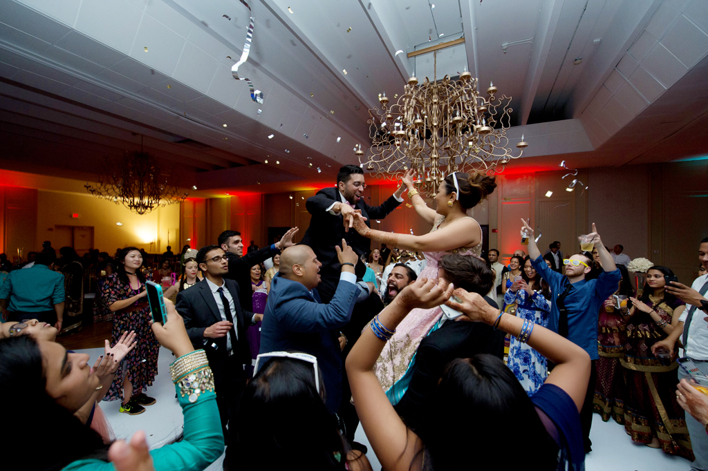 wedding guests hold up the bride and groom and shoot confetti during an indian wedding reception