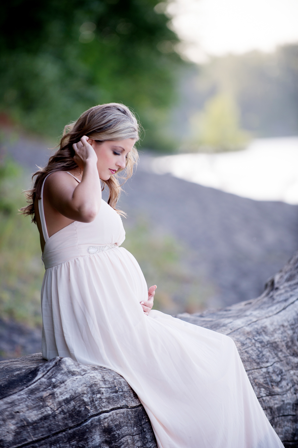 a pregnant woman sits on a log by the river
