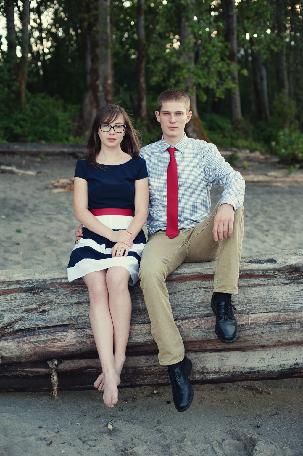 a couple wearing red white and blue sit on a fallen log in the sand