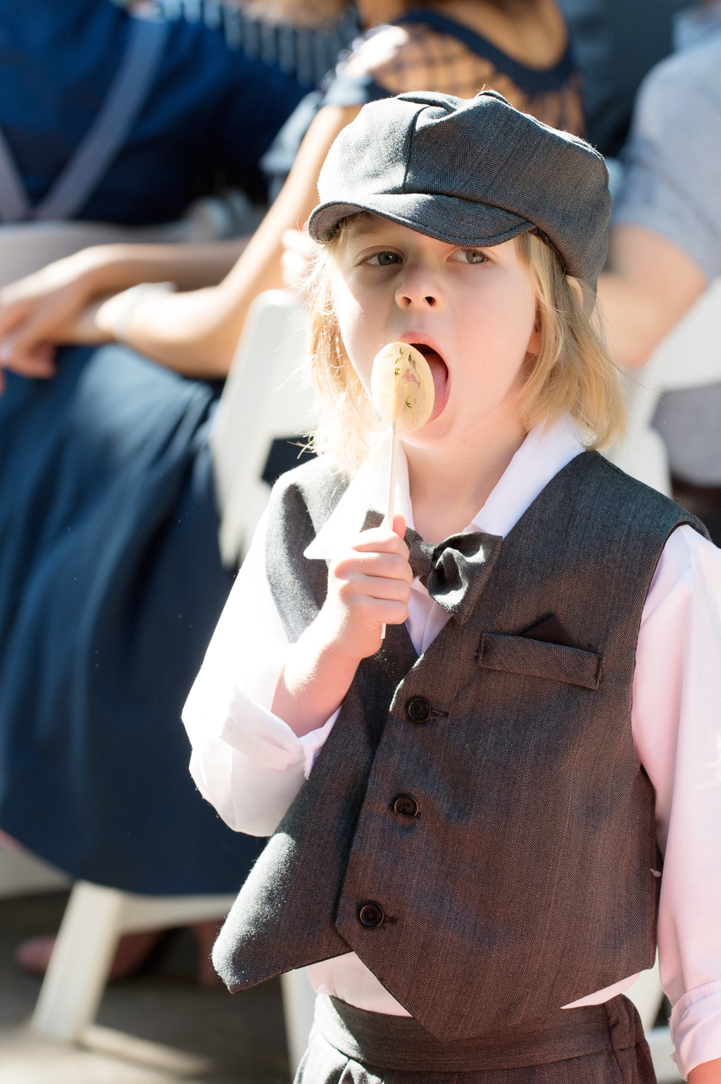 a young boy in a page boy cap licks a lollipop
