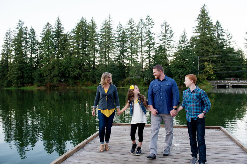 a family in yellow and blue hold hands and walk on the dock at lacamas lake