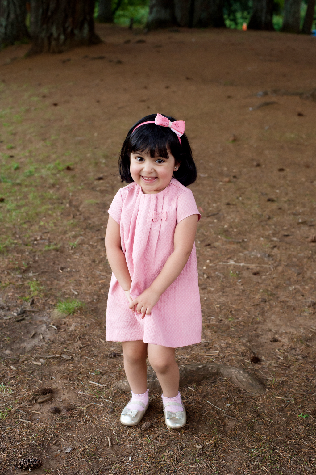 a little girl in a pink dress smiles shyly at the camera