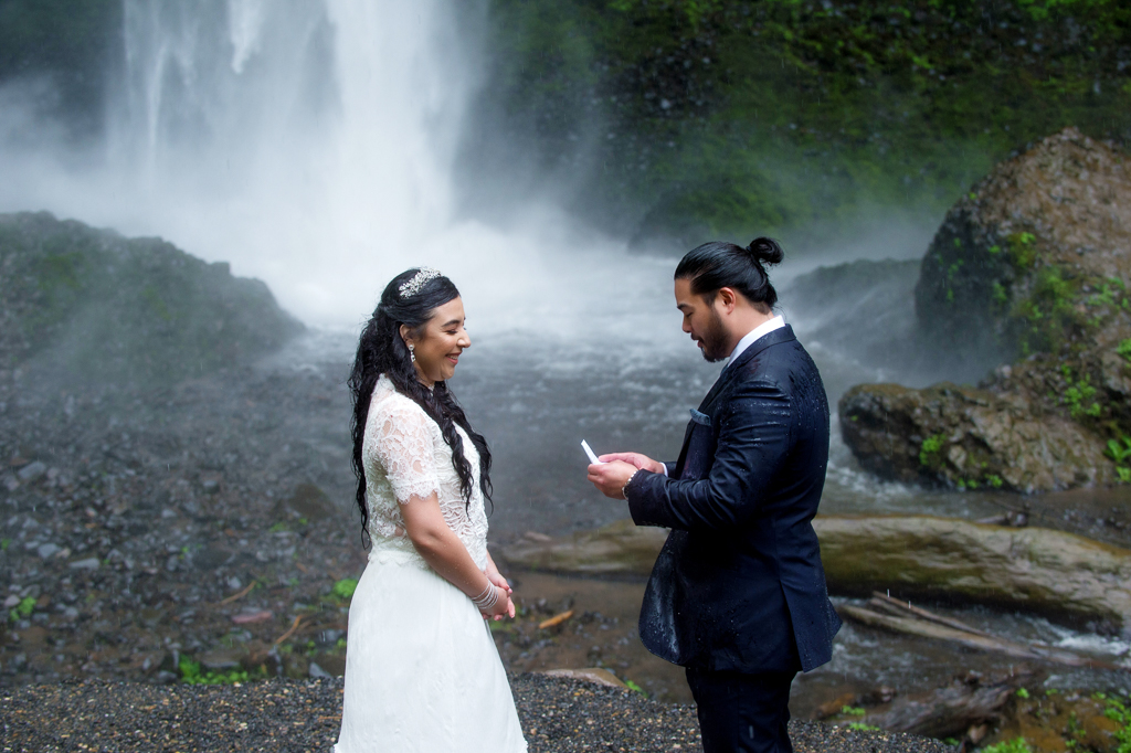 a groom reads his wedding vows to the bride in front of a waterfall