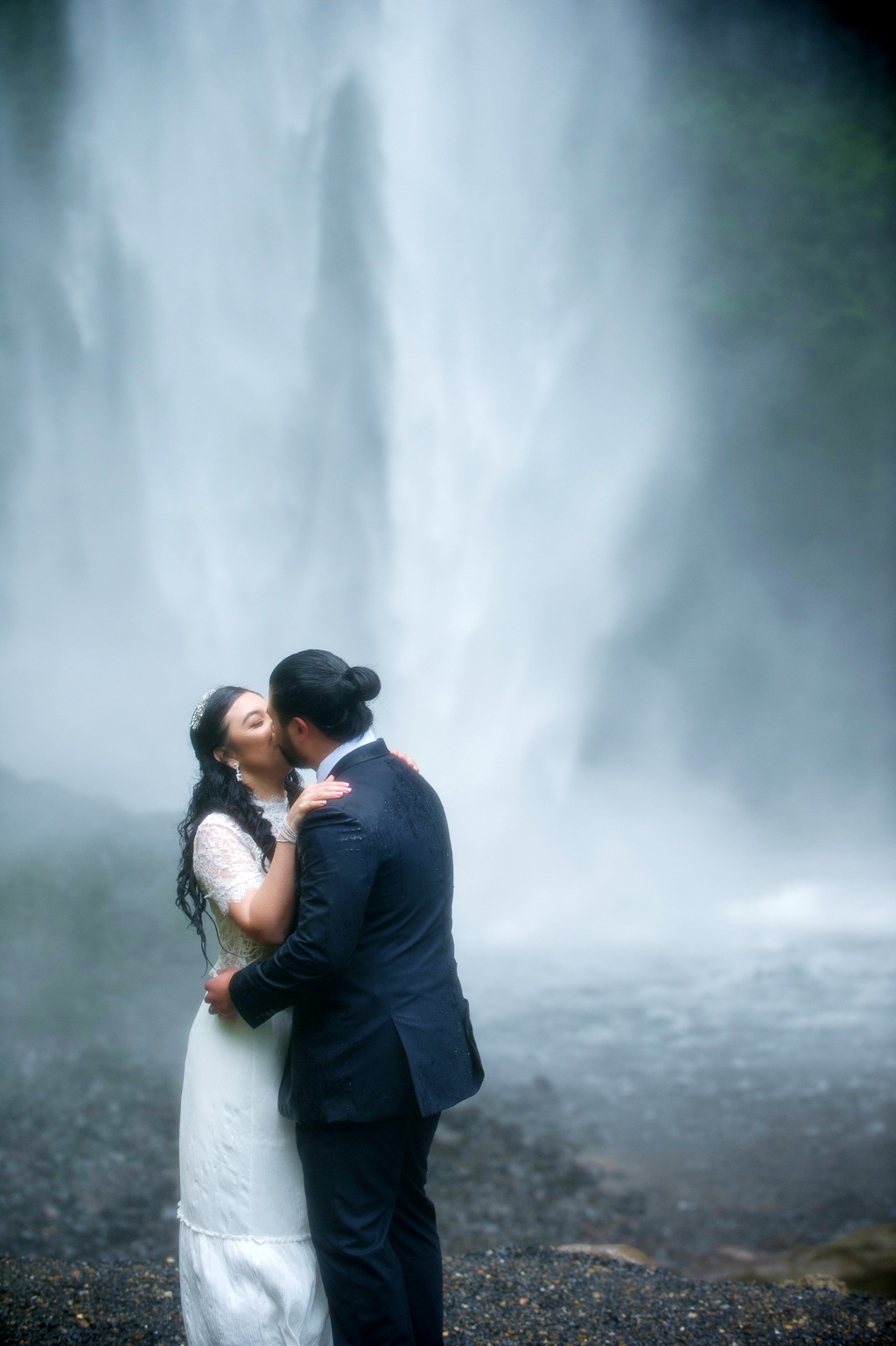 a rain soaked bride and groom kiss in front of a waterfall after their elopement