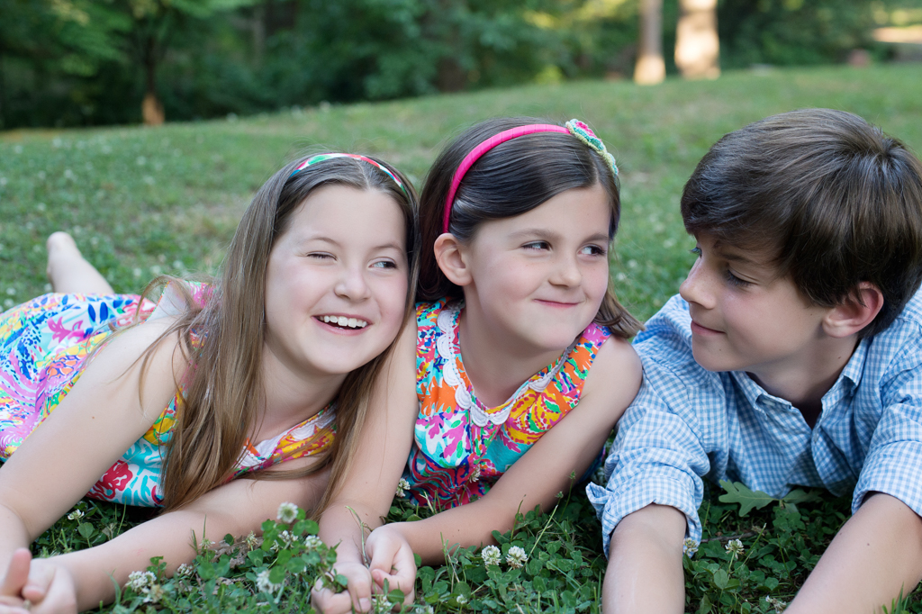 3 siblings lay on their bellies in the grass