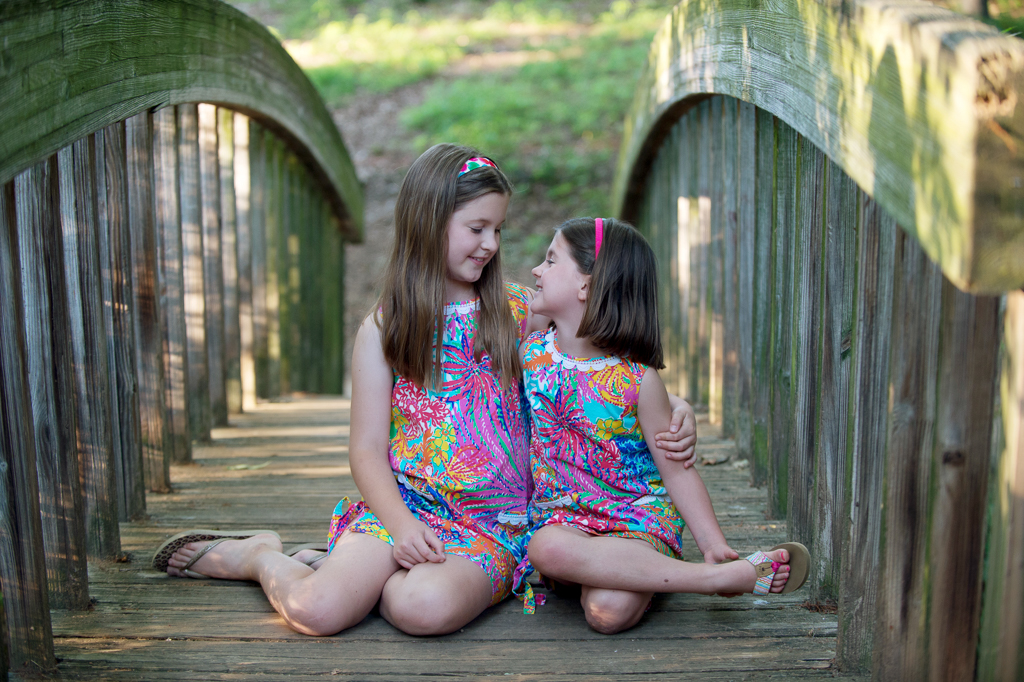 sisters look at each other while sitting on a wooden bridge