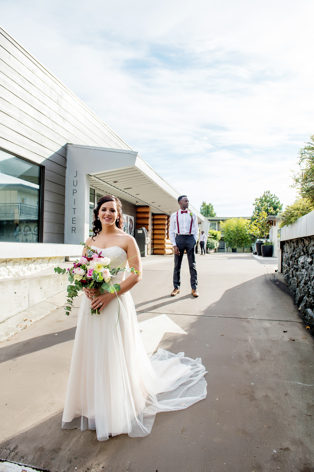 bride stands in driveway of the jupiter hotel while groom stands in background