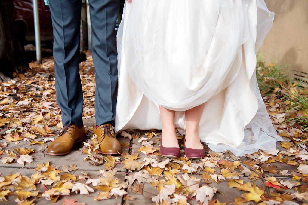 bride and groom's feet stand in fallen autumn leaves