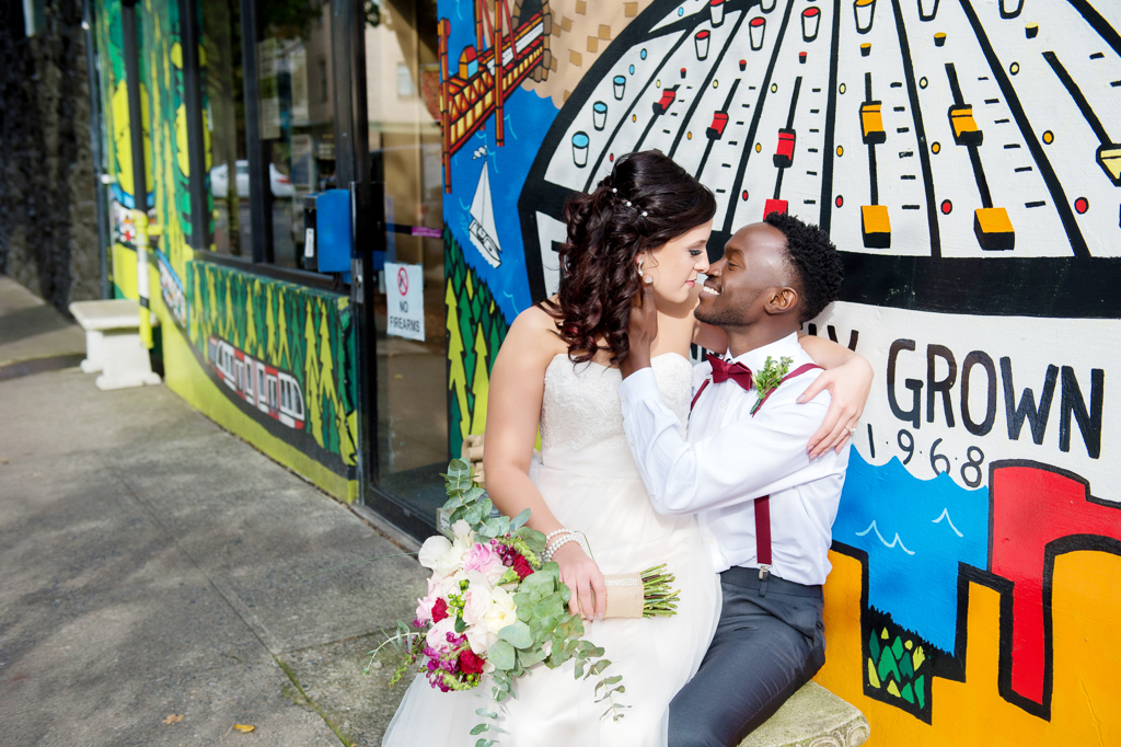 bride sits in groom's lap and kiss in front of bright mural along burnside
