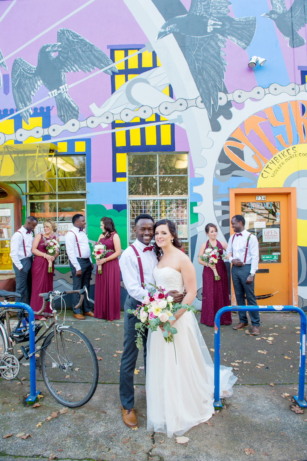 the wedding party wearing maroon stand under a brightly colored mural near burnside