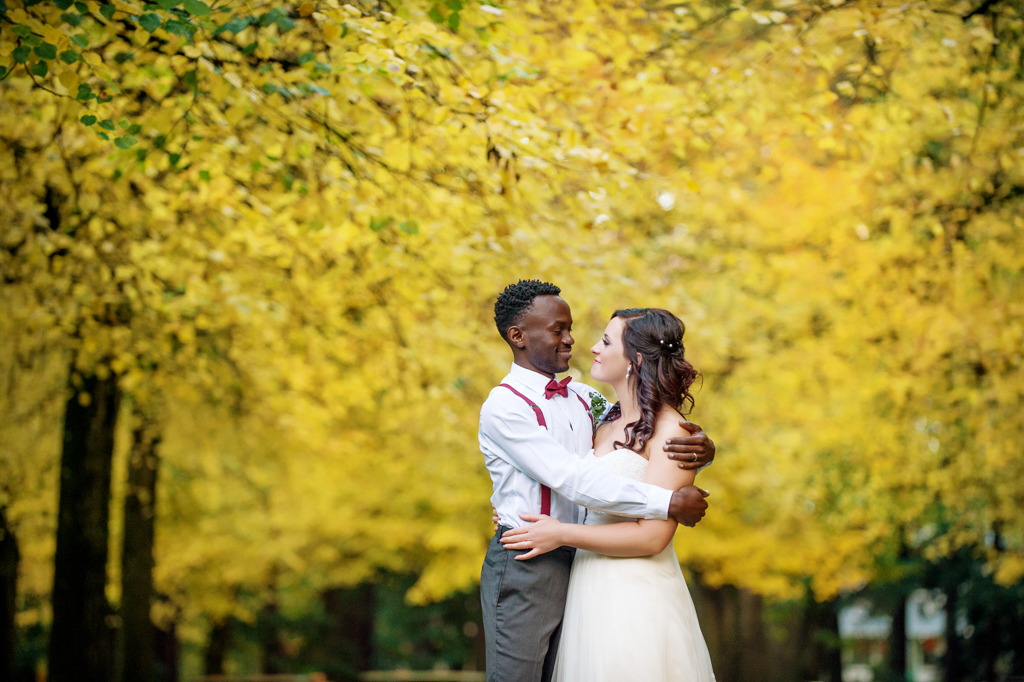 bride and groom embrace underneath a large bright yellow autumn tree