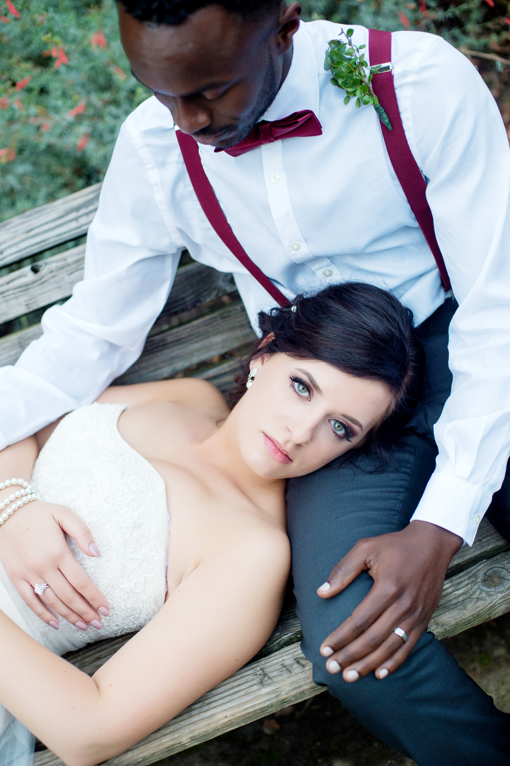 bride with bright blue eyes lays head in grooms lap on a bench and looks intently at the camera