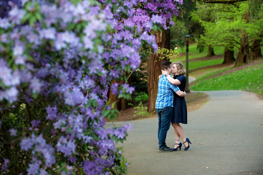 purple flowers frame a couple kissing at a park