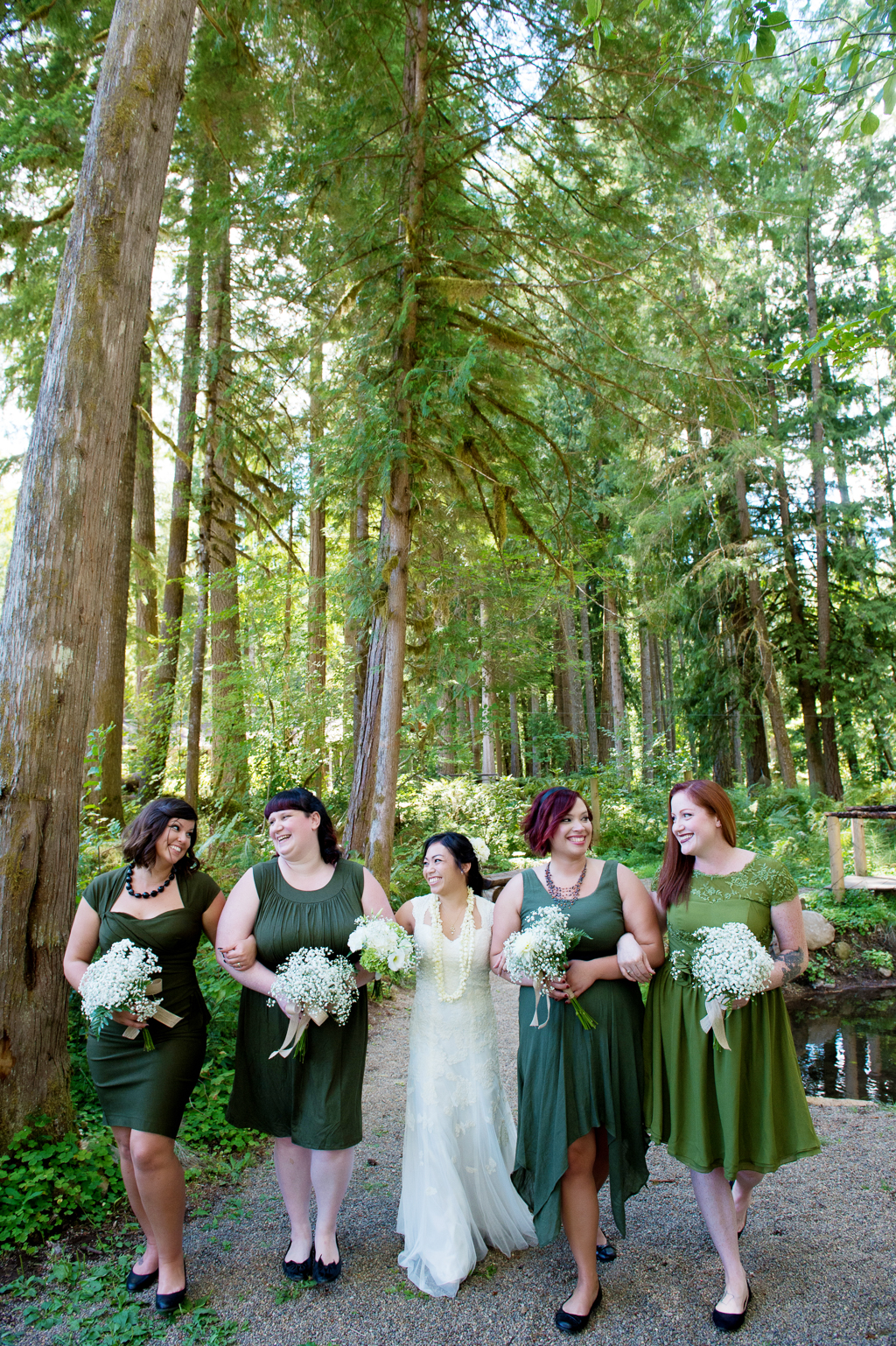bridesmaids wear mismatched green dresses and walk in the forest with the bride