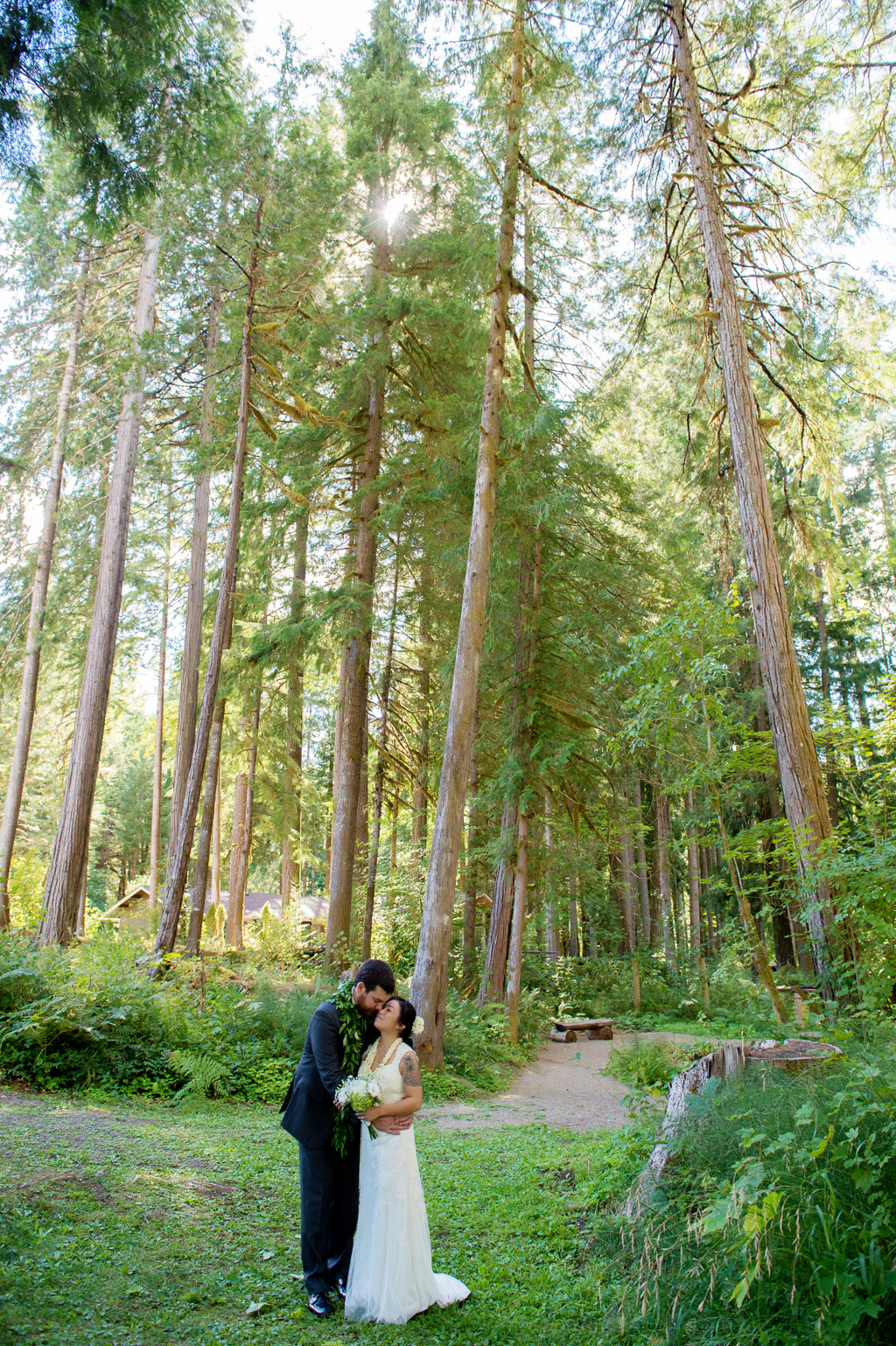 a bride and groom kiss under tall forest trees
