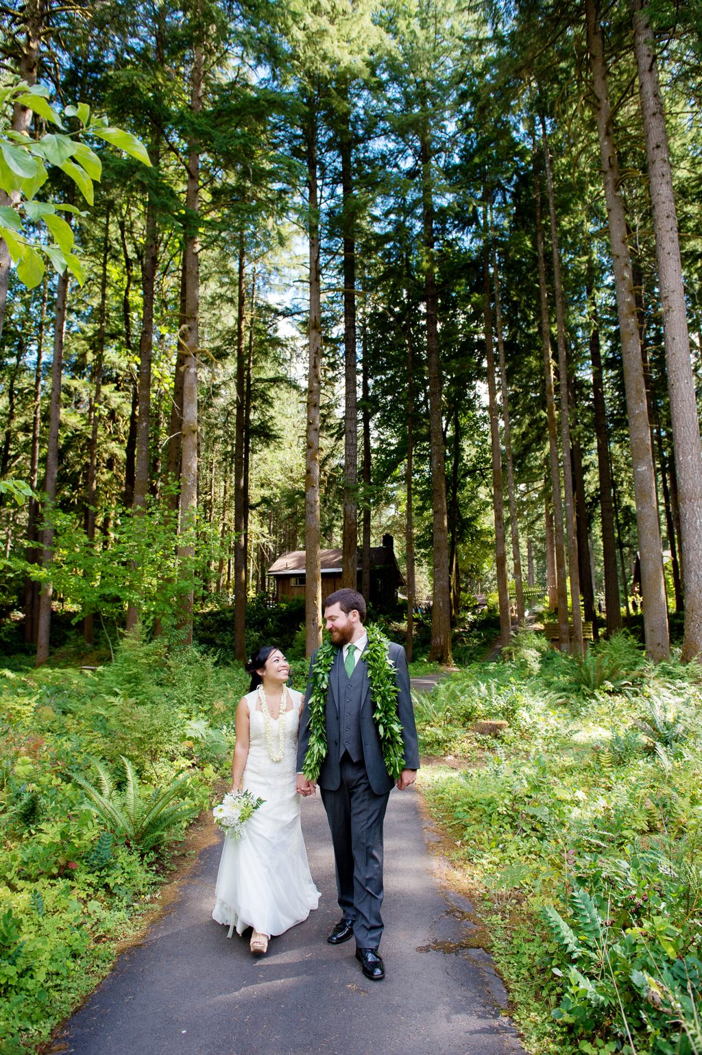 a bride and groom walk down a trail under tall trees
