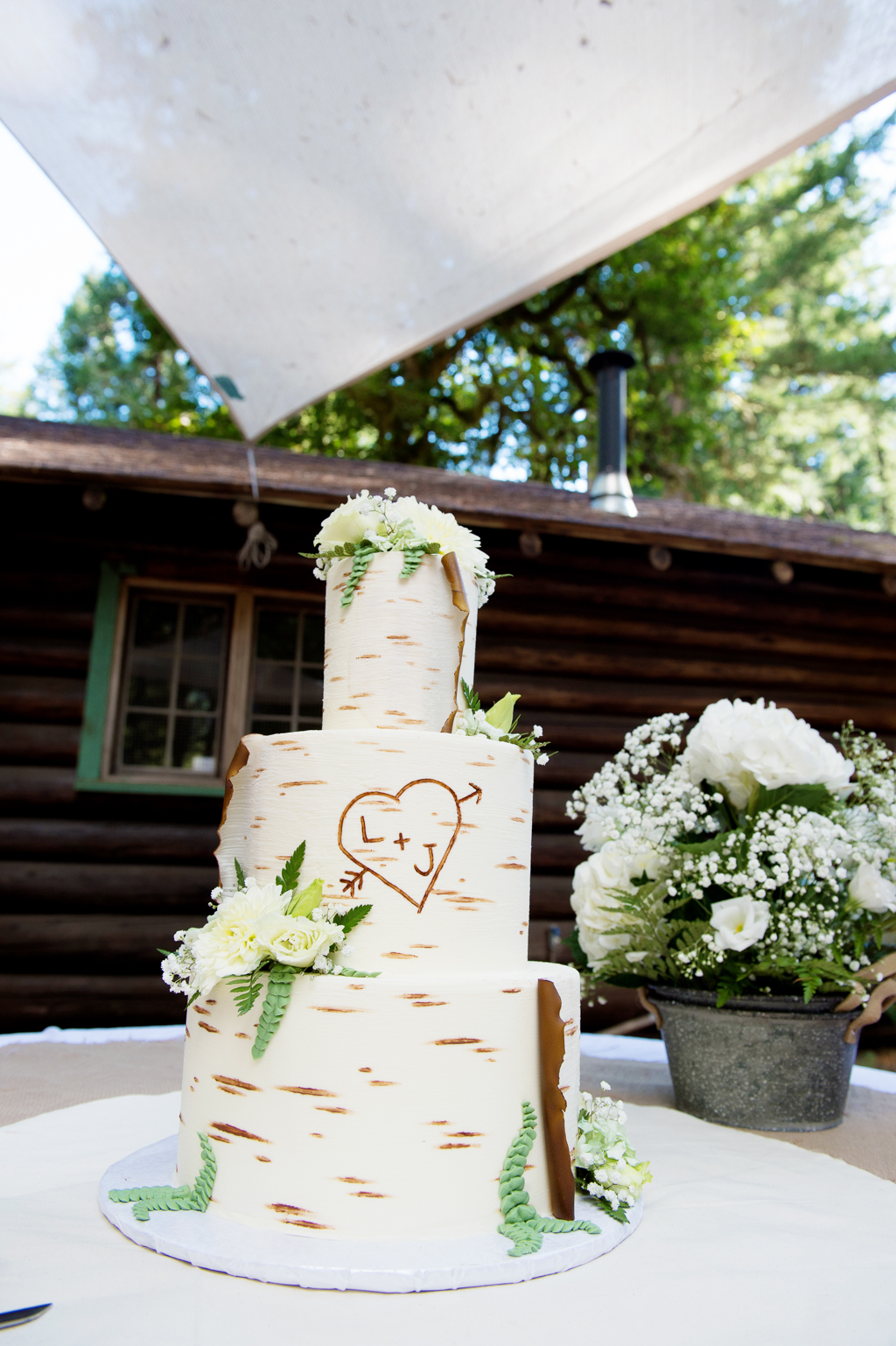 a 3 tier wedding cake decorated to look like white birch bark and carved with a heart