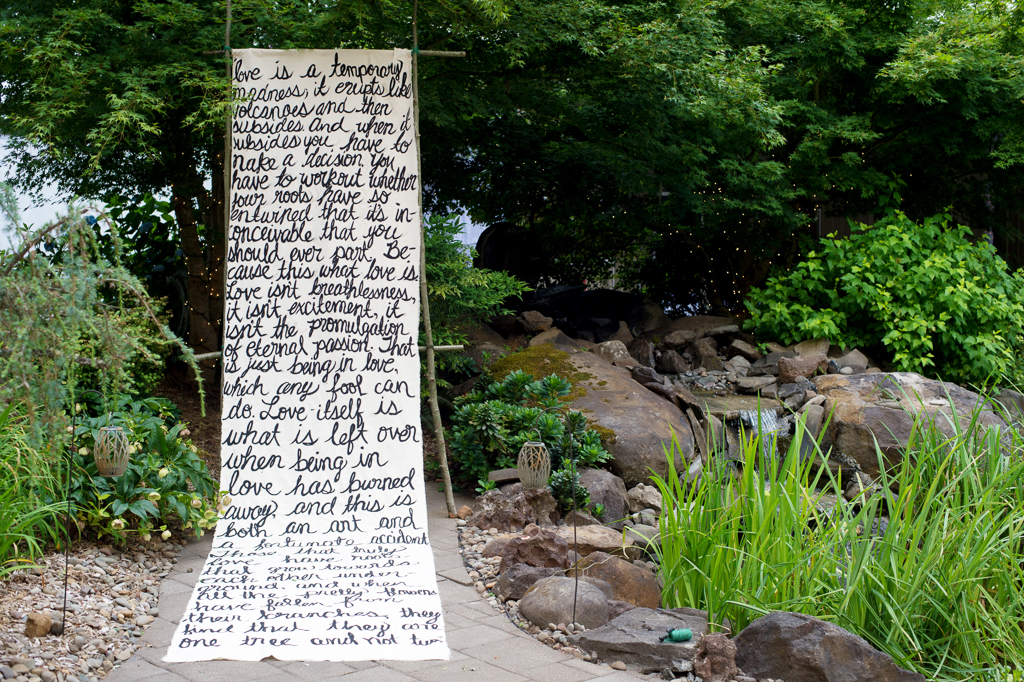 a poem written on muslin hangs as the backdrop for the Thorburg Oasis wedding ceremony arbor 