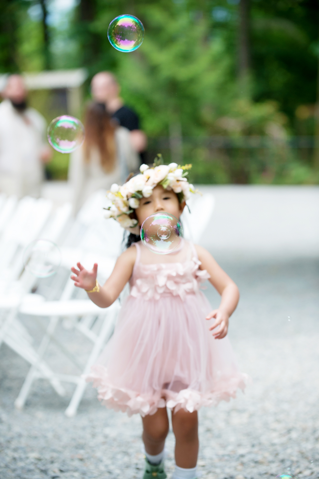 a flower girl in a pink dress and a flower crown chases a bubble