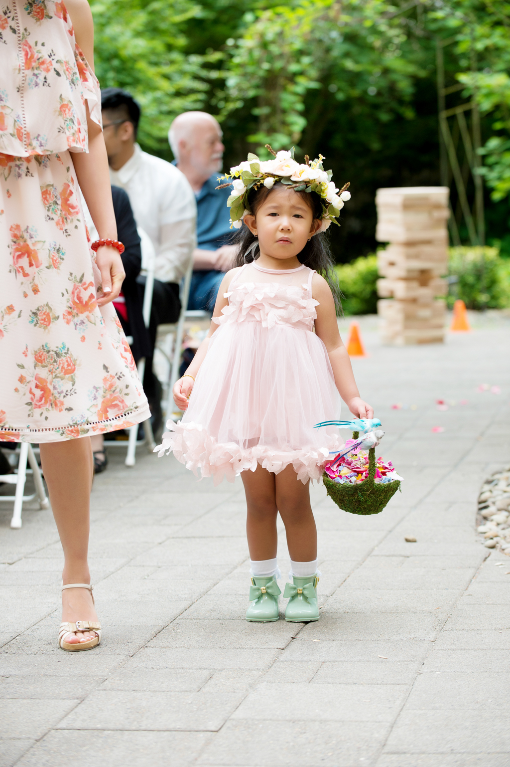 a flower girl wearing a pink dress a flower crown and green rain boots walks down the aisle
