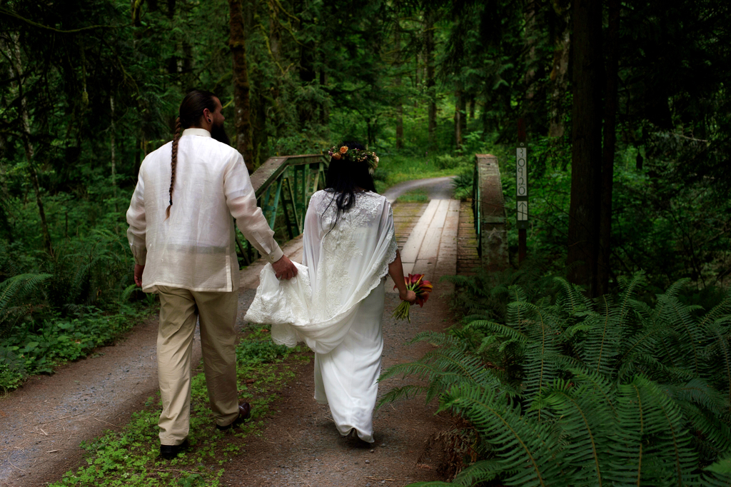 a bride and groom walk through a dark forest towards a bridge