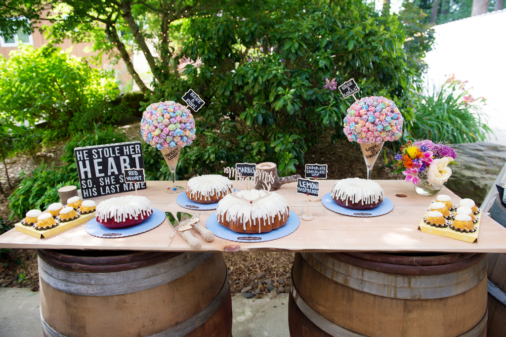 several bundt cakes with white icing and dumdum lollipop trees decorate a dessert table at a wedding