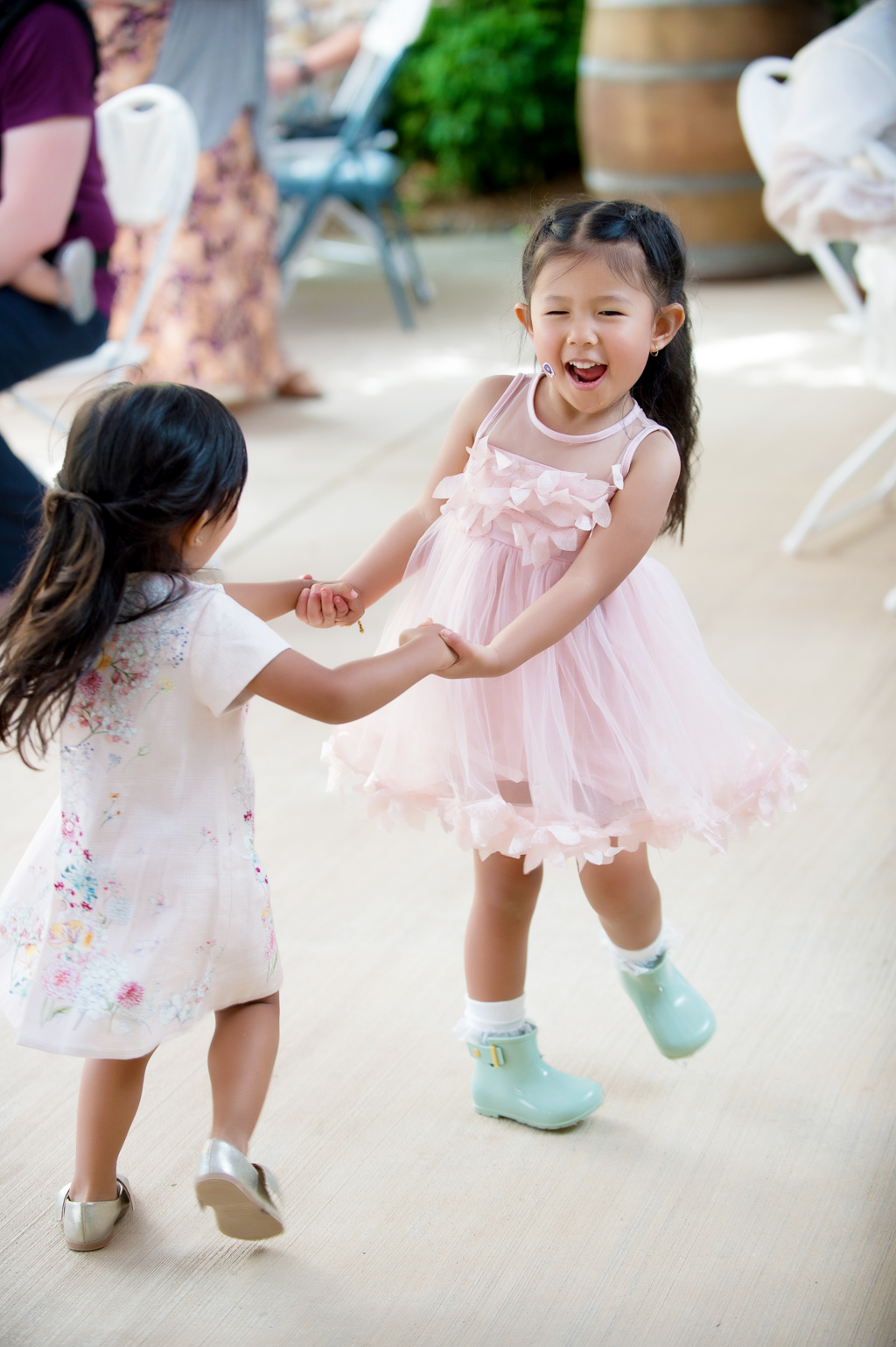 a flower girl in a pink dress and mint green rain boots dances with another girl during the wedding reception