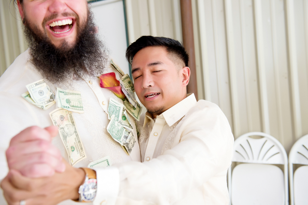 a groom has dollar bills pinned to his shirt during the money dance as a man dances with him