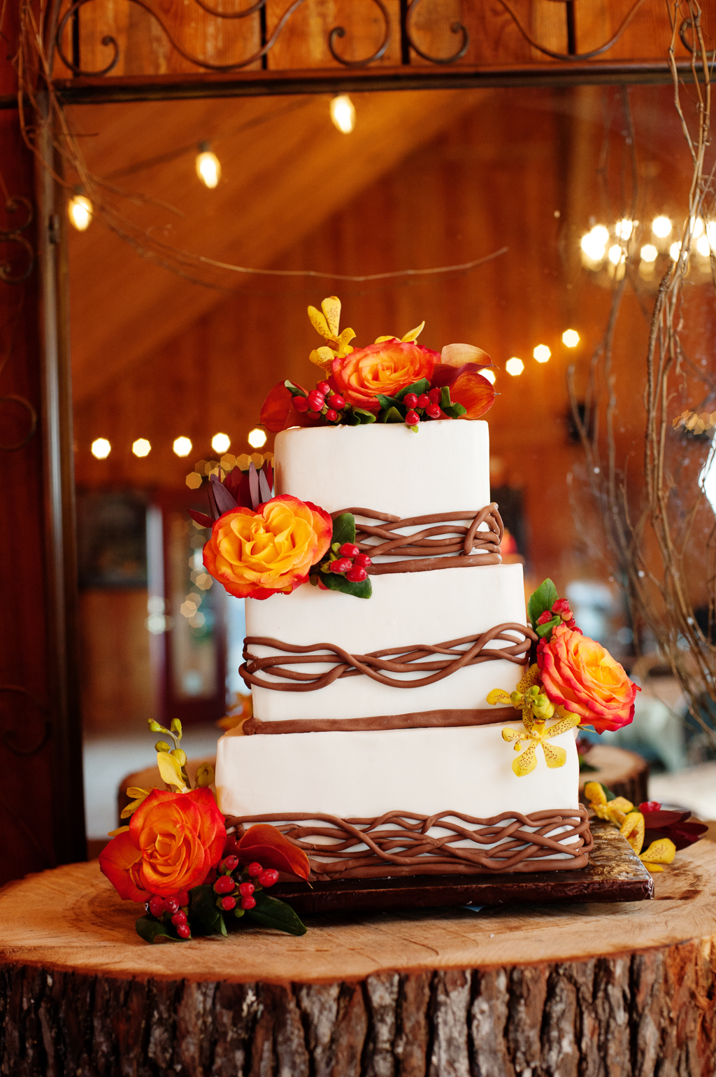 a white wedding cake with brown icing and large orange and yellow flowers