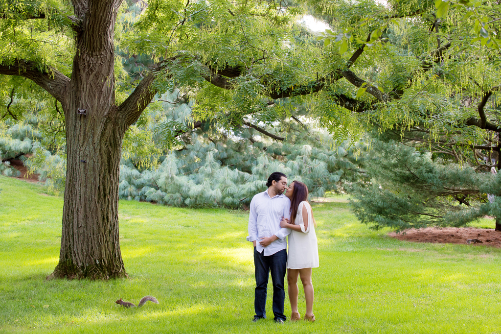 a couple kiss under a tree at new york botanical garden as a squirrel scurries past